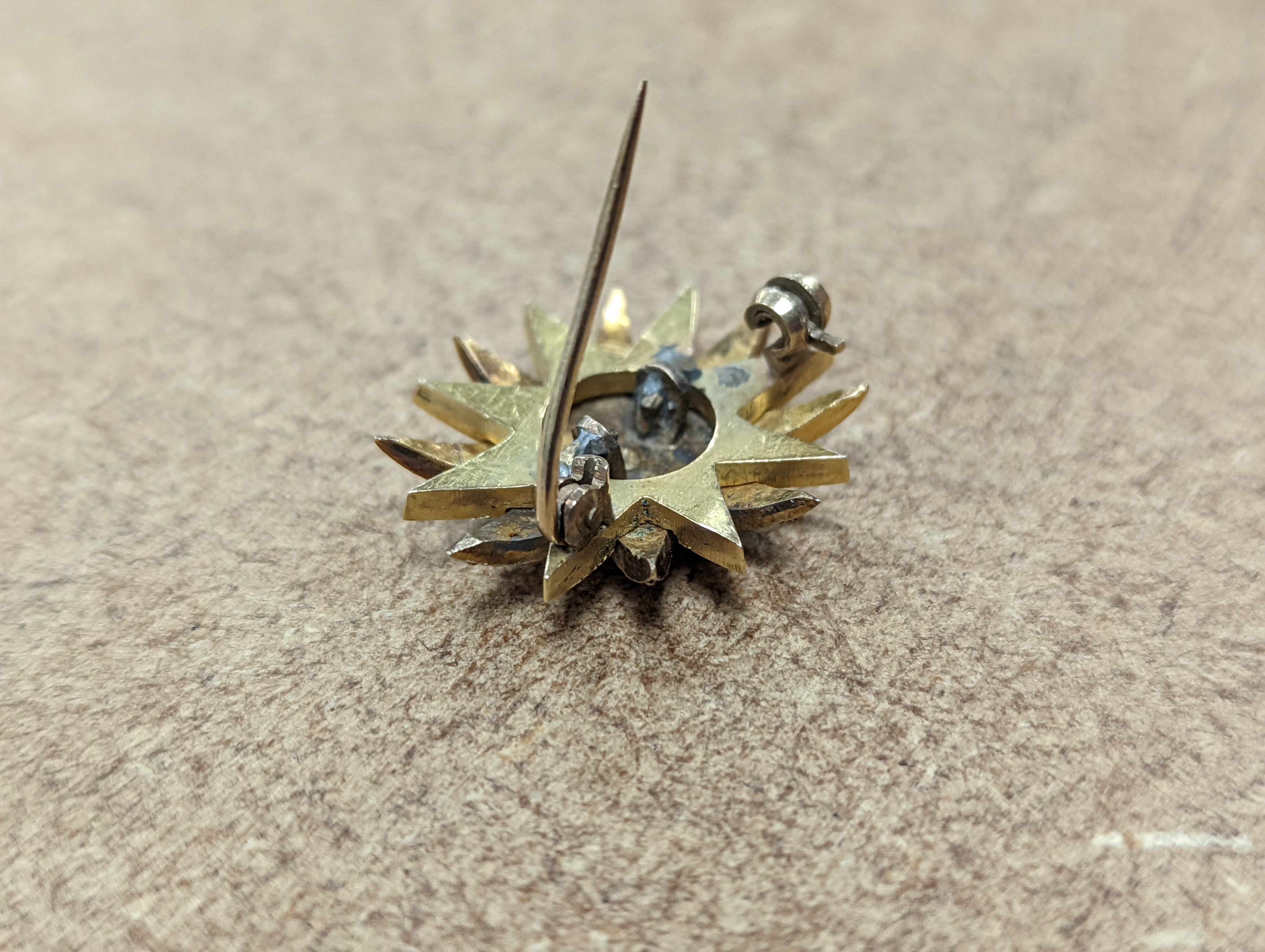 An Edwardian yellow metal, graduated split pearl and single stone diamond set starburst brooch(adapted?), 24mm, gross weight 6.5 grams.